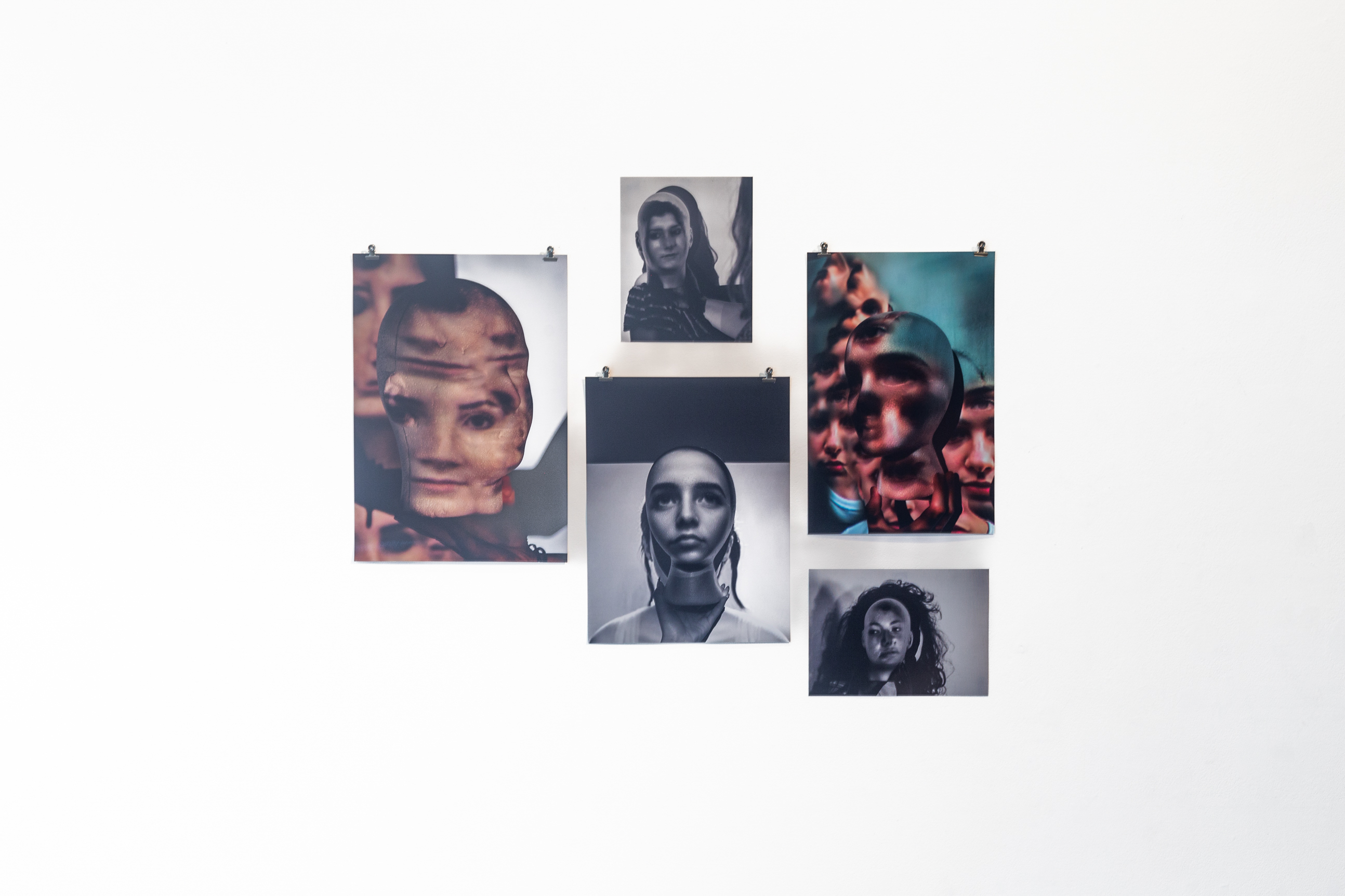 Five printed posters arranged on a white wall, each print consisting of experimental photography of faces.